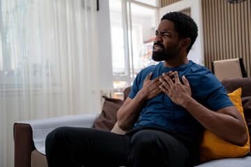 Young man suddenly feeling chest pain heart attack sitting in living room