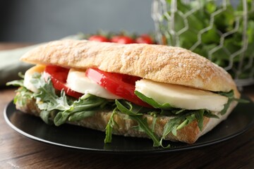 Delicious sandwich with mozzarella cheese, tomato and arugula on wooden table, closeup