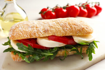 Delicious sandwich with mozzarella cheese, tomatoes and arugula on table, closeup