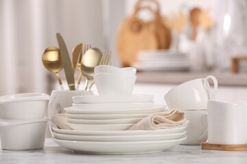 Different clean white dishware, cups and cutlery on marble table indoors