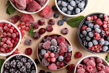 Different ripe frozen berries and mint leaves on light wooden table, flat lay