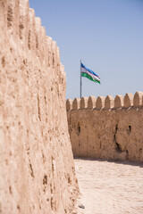 View along the ancient mudbrick walls of Khiva, Uzbekistan, with the national Uzbek flag visible in the distance