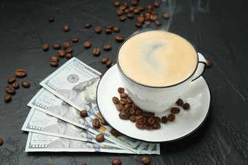 Cup of aromatic coffee, dollar banknotes and roasted beans on dark textured table, closeup