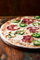 Pizza with salami, mozzarella cheese and jalapeno pepper. Wooden background. Soft focus.  