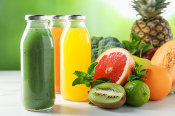 Tasty juices in glass bottles, fresh ingredients and mint on white table against blurred green background, closeup