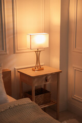 Bedside table with lamp near bed indoors