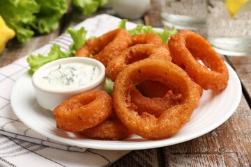 Fried squid rings served with sauce on wooden table, closeup