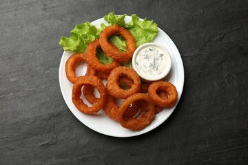 Fried squid rings served with sauce on black table, top view