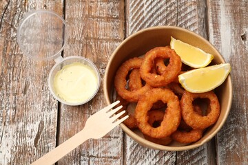 Fried squid rings, lemon and sauce on wooden table, flat lay