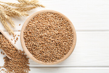 Wheat grains in bowl, scoop and spikelets on white wooden table, flat lay. Space for text