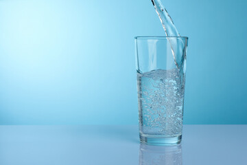Pouring refreshing soda water into glass at light grey mirror table against turquoise gradient background, closeup. Space for text