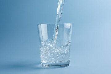Pouring refreshing soda water into glass on light blue gradient background, closeup