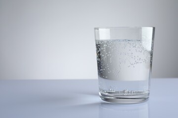 Refreshing soda water in glass on white mirror table against grey gradient background, closeup. Space for text