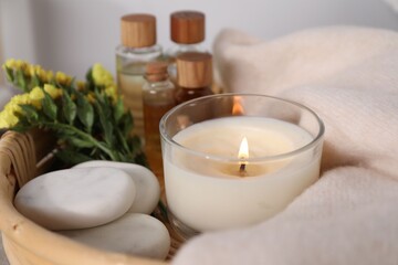 Spa composition with burning candle and flowers in tray, closeup