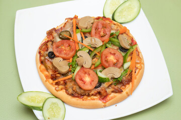 Vegetable and mushroom pizza garnished with fresh cucumber and carrots on a plate side view of Bangladeshi food