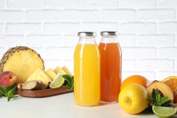 Tasty juices in glass bottles, fresh fruits, ginger and mint on white table against brick wall