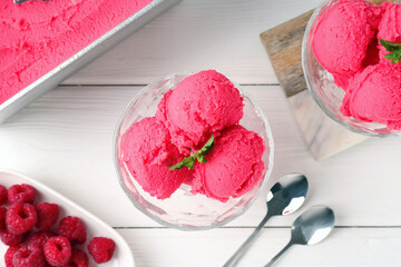 Delicious raspberry sorbet with mint in dessert bowls, spoons and fresh berries on white wooden table, flat lay