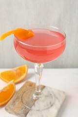 Martini cocktail with garnish and slices of orange on white table, closeup