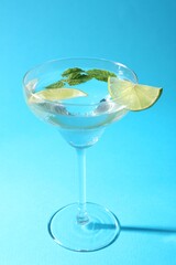Martini cocktail with slices of lime and mint on light blue background, closeup