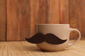 Happy Father's Day. Cup with mustache on wooden table, closeup. Space for text
