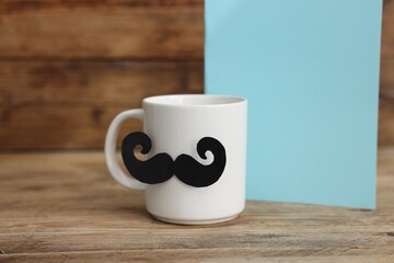 Happy Father's Day. Cup with mustache and card on wooden table. Space for text