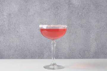 Martini cocktail with sugar in glass on white table near grey wall, closeup
