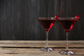 Martini cocktail with cherries in glasses on wooden table, closeup. Space for text
