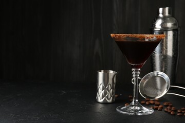 Martini cocktail with sugar in glass, coffee beans and shaker on black table, closeup. Space for text