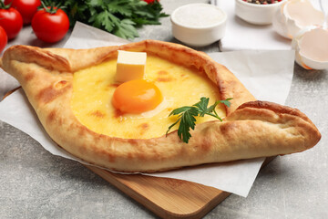 Tasty khachapuri with cheese, egg, parsley and other products on light grey background, closeup