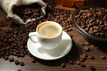 Aromatic coffee in cup and beans on wooden table, closeup