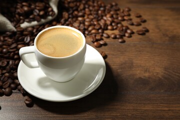 Aromatic coffee in cup and beans on wooden table, closeup. Space for text
