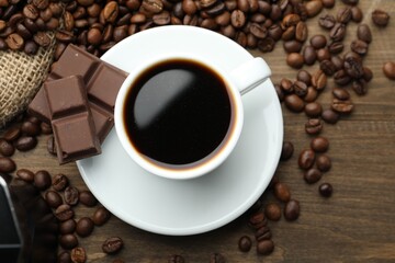 Aromatic coffee in cup, beans and pieces of chocolate on wooden table, flat lay