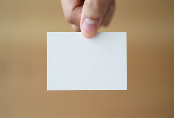 Hand holding a blank white square card against a textured brown background
