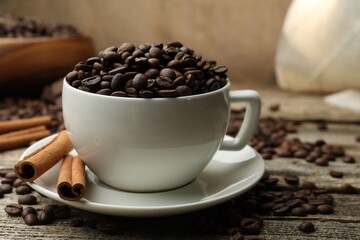 Aromatic coffee beans in cup and cinnamon on wooden table, closeup