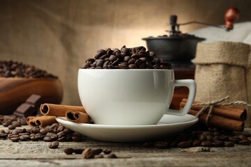 Aromatic coffee beans in cup, cinnamon and grinder on wooden table, closeup