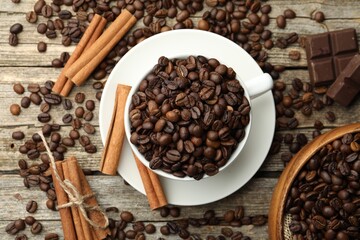 Obraz premium Aromatic coffee beans in cup, cinnamon and pieces of chocolate on wooden table, flat lay