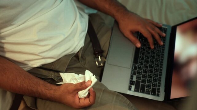 Tissues on hand Man masturbate watching adult video on the bed with only tissues around him. Loneliness man watching porn site video on a laptop.