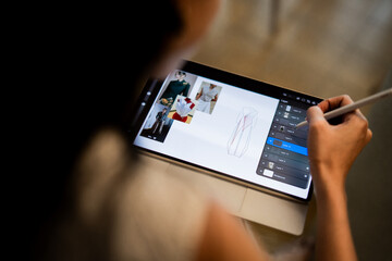 A designer uses a digital tablet and stylus to create fashion sketches with dress patterns and fabric inspiration, highlighting modern design technology