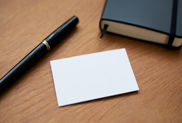 Blank business card and pen on a wooden desk next to a notebook