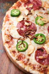 Pizza with salami, mozzarella cheese and jalapeno pepper. Wooden background. Soft focus.