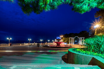 Gelendzhik resort embankment in the evening. There is a musical fountain in the center. Behind it is a colonnade. Balustrade along the sea line