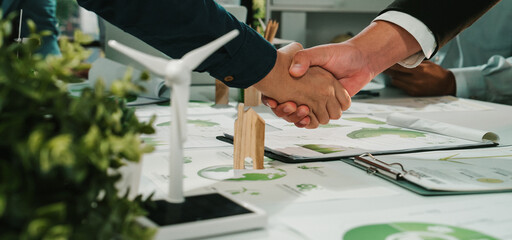 This image captures the moment of a business agreement focused on sustainability, featuring a handshake and green energy models, symbolizing collaboration in eco-friendly practices. SACTR © InfiniteFlow