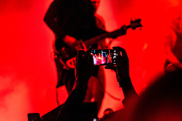 Capturing live music magic, fans record energetic concert performance with smartphones under vibrant red stage lights