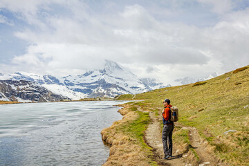Fototapeta premium Hiker by Mountain Lake with Snowy Peaks