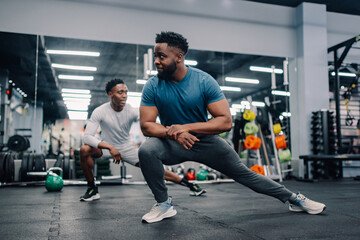 Two male athletes stretching legs in modern gym