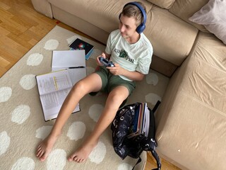 Teen boy struggles to focus on homework while holding a game controller. A realistic moment illustrating attention challenges, possibly linked to ADHD.
