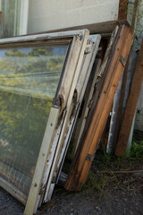 Old dirty window frames stacked on the ground next to a wall. Visible damage, peeling paint, and abandoned glass panes symbolize urban waste and lack of proper recycling. 