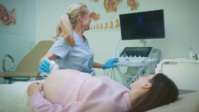 Experienced doctor performing ultrasound scan for pregnant woman lying on bed. Specialist operating new machine while looking at monitor. Medical examination in modern clinic room.
