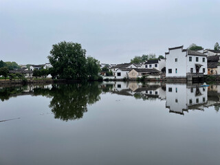 Fototapeta premium Tranquil scene of a Chinese village with traditional architecture reflecting in calm water.
