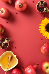 Rosh Hashanah still life. Flat lay of apples, pomegranates, sunflower, and honey in yellow apple-shaped dish on red background